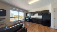 Located at 401 S Main St in the heart of downtown Akron, Ohio, this studio unit offers a well-organized, open-concept floor plan that efficiently combines living, dining, sleeping, and cooking areas in a single cohesive space. Warm hardwood-style flooring runs throughout the main living area, adding a sense of continuity and warmth.

The kitchen is a standout feature, equipped with dark espresso cabinetry that extends to the ceiling for ample storage, granite-style countertops, and a full suite of black appliances including an electric range, built-in microwave, dishwasher, and refrigerator. The kitchen flows seamlessly into the living and dining area, which benefits from a large picture window that frames views of the surrounding downtown Akron streetscape and fills the space with natural light. The living area accommodates a sofa, coffee table, wall-mounted television, and a compact dining set positioned near the window.

The sleeping area is situated within the open layout, offering a closet for storage. The bathroom is finished with earthy slate-toned tile flooring, a dark vanity, and a full tub-shower combination. A textured ceiling is consistent throughout the unit. The space is practical and functional, well-suited for urban living in a central Akron location.