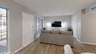 Located at 9401 Mixon Dr in Dallas, TX, this one-bedroom, one-bathroom unit offers a thoughtfully designed single-floor layout that maximizes every square foot. The open-concept living, dining, and kitchen area creates a seamless flow ideal for both relaxing and entertaining. The living room features wood-look flooring, neutral gray walls, and large windows that invite abundant natural light, while also providing a dedicated workspace area. The kitchen is well-equipped with stainless steel appliances—including a refrigerator, gas range, and microwave—paired with white cabinetry and a light stone countertop with an integrated sink. The adjoining dining area comfortably accommodates a round table and chairs. The spacious bedroom includes a ceiling fan, wood-look flooring, and a sliding glass door that opens to an outdoor patio with exterior views. Two closets provide generous storage throughout the unit. The bathroom features white subway tile, a tub/shower combination, and a clean vanity with ample counter space. A hallway connects the living areas to the private quarters, completing this well-organized and modern Dallas residence.