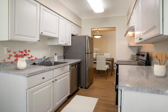 Renovated Package I kitchen featuring stainless steel appliances, white cabinetry, grey laminated countertops, and hard surface flooring - Tysons Crossing