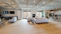 This single-story clubhouse is designed to provide an upscale communal gathering space with a cohesive, contemporary aesthetic throughout. The main lounge area is immediately striking, anchored by a floor-to-ceiling stacked stone fireplace flanked by large windows dressed with woven bamboo shades, allowing ample natural light to fill the room. Coffered ceilings with recessed lighting add architectural depth and a sense of grandeur to the space. Wide-plank hardwood flooring runs seamlessly throughout, contributing to a warm, unified atmosphere.

Multiple seating arrangements are thoughtfully distributed across the lounge, offering flexible areas for both intimate gatherings and larger social events. A secondary lounge area features direct access to the outdoors through glass-paned French doors. The kitchen is well-appointed with white shaker cabinetry, granite countertops, stainless steel appliances, double wall ovens, and a bold geometric tile backsplash that adds a modern accent.

A dedicated dining area, lined with oversized windows overlooking the pool, seats a large group comfortably and is bathed in natural light. The overall ambiance of the clubhouse is polished and welcoming, balancing refined design details with functional, community-oriented spaces.