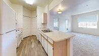 Located at 3601 S Dallas St in Aurora, CO, this two-bedroom, one-bathroom residence offers a functional and well-organized single-floor layout. The open-concept living area seamlessly connects the kitchen, dining, and living spaces, creating a bright and cohesive environment. The kitchen features a peninsula with a built-in double sink, light wood cabinetry with gold-tone hardware, white appliances including a refrigerator and electric range, and a dedicated pantry for added storage. The living area is finished with plush carpeting and benefits from multiple windows that invite natural light throughout the space. Both bedrooms are carpeted and offer a calm, neutral palette with windows providing outdoor views; the primary bedroom includes access to a walk-in closet with built-in shelving and hanging rods. A second closet provides additional storage. The full bathroom is finished with wood-look vinyl flooring, a single vanity with a large mirror and a well-lit fixture bar above, and a tub-shower combination. Neutral tones are carried throughout the unit, giving the space a clean, move-in-ready appearance. The layout is practical and efficient, making excellent use of the available square footage.
