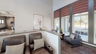 This single-story community space in Fort Mill, SC, is thoughtfully designed to blend contemporary aesthetics with warm, inviting elements. The layout encompasses several distinct functional zones that flow naturally into one another, creating a cohesive and versatile gathering environment.

At the heart of the space is a well-appointed wet bar and kitchenette area, featuring rich walnut cabinetry, white subway tile backsplash, granite countertops, stainless steel appliances, and open shelving for display. A substantial granite-topped island with bar seating serves as a central gathering point, complemented by a wall-mounted television for entertainment.

Adjacent to the kitchenette, a lounge area offers comfortable leather reclining seating and a half-wall with granite ledge, lending a tiered, theater-like feel. High ceilings with recessed lighting contribute to the open, airy atmosphere throughout.

A cozy seating nook near large windows features two upholstered armchairs and provides views of an outdoor pool area, allowing natural light to fill the space. A striking reclaimed wood barn door with a chevron pattern serves as both a functional divider and a bold design statement, adding rustic character against the otherwise modern backdrop. Light wood-look tile flooring unifies the entire space.