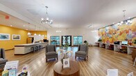 Located at 3085 Highway 123 in San Marcos, Texas, this well-appointed single-story space offers a generous, open floor plan designed to accommodate both collaborative and individual activities. The interior is characterized by warm hardwood flooring, soaring vaulted ceilings, and abundant recessed lighting that creates a bright, welcoming atmosphere throughout.

The kitchen area is a standout feature, showcasing a large island with a mosaic tile base and white quartz countertop, complemented by pendant lighting and bold golden-yellow walls adorned with a curated gallery of botanical artwork. White cabinetry, a stainless steel sink, and full-size appliances complete the functional yet stylish space, with bar-height stools providing casual seating along the island.

The living and common areas offer flexible seating arrangements, including lounge chairs and small café-style tables, making the space ideal for both relaxation and productivity. A dedicated workstation zone features a striking floor-to-ceiling geometric mural in vivid multicolored tones, built-in desks, and an elegant chandelier, alongside natural light streaming through large windows with outdoor views.

The office area includes warm wood-toned desks, coordinating accent chairs, and framed landscape artwork, contributing to a professional yet inviting feel. Throughout the space, thoughtful design details — from decorative chandeliers to curated wall art — create a cohesive, energetic, and functional environment.