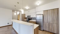 This single-floor, one-bedroom, one-bathroom residence offers a thoughtfully designed layout that balances comfort and functionality. The open-concept kitchen and living area serves as the heart of the home, featuring a large waterfall-edge island with a crisp white countertop, two-tone cabinetry combining white upper cabinets with warm wood-toned lower cabinets, a mosaic tile backsplash, and a full suite of stainless steel appliances including a refrigerator, range, and microwave. Stylish pendant lighting illuminates the kitchen, while light wood-tone flooring extends throughout the main living area, which benefits from abundant natural light through large windows and French doors that open to the outdoors. The bedroom is a comfortable retreat finished with plush carpet and a window that brings in natural greenery views. A dedicated closet provides ample storage. The bathroom is finished with clean, modern wood-grain cabinetry, a tall storage tower, and neutral flooring for a spa-like feel. A private in-unit laundry room houses a full-size front-loading washer and dryer with overhead shelving. The hallway, accented by louvered doors and warm wood trim, connects all spaces efficiently, completing this well-organized and move-in-ready home.