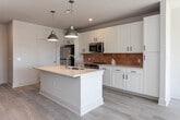 Located at 215 Willow Ave in Knoxville, Tennessee, this thoughtfully designed single-floor residence combines modern aesthetics with functional living. Light-toned hardwood flooring runs throughout the unit, creating a bright and cohesive feel from room to room.

The open-concept kitchen is a standout feature, anchored by a large center island with a double undermount sink and light quartz countertops. White shaker-style cabinetry reaches toward the ceiling, complemented by a warm terracotta tile backsplash that adds a distinctive pop of color. Stainless steel appliances — including a refrigerator, electric range, and built-in microwave — complete the kitchen. Industrial-style pendant lights hang above the island, adding character to the space.

The living area extends naturally from the kitchen and is bathed in natural light from large windows and a glass door that opens to a private balcony, offering views of the surrounding Knoxville cityscape. Ceiling fans are present in both the living and bedroom areas for added comfort.

The bedroom is generously sized with an en suite bathroom featuring large-format tile surrounding a soaking tub and shower combination, a white vanity, and clean, neutral finishes. An in-unit laundry area with a top-load washer and overhead wire shelving provides added convenience.