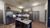 This single-story residence at 950 FM-156 in Justin, Texas, offers a thoughtfully designed interior with contemporary finishes and a cohesive neutral-and-navy color palette. The kitchen serves as a central highlight, showcasing dark espresso cabinetry, a white subway tile backsplash, granite countertops, and stainless steel appliances including a refrigerator, range, microwave, and dishwasher. A granite-topped island with seating provides additional workspace and a casual dining option, while pendant lighting overhead adds a refined touch. Wood-look flooring runs throughout the main living areas, contributing warmth and continuity.

The living room is generously proportioned, featuring a ceiling fan, large windows that admit natural light, and access to an exterior door. A bold navy accent wall anchors the space and complements the neutral tones of the surrounding walls. The bedrooms continue the navy accent theme, with carpet flooring and windows for natural light. Each bathroom is finished with granite countertops, dark cabinetry, and wood-look flooring, with at least one bathroom offering direct access to a walk-in closet. Overall, the space presents a modern, well-coordinated aesthetic suited to comfortable everyday living.