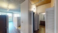 Located at 707 Tenth Ave in the heart of San Diego, CA, this third-floor unit offers a compelling blend of industrial design and modern finishes. The space is defined by its striking exposed concrete ceilings, which lend an authentic urban loft character throughout. Hardwood-style flooring runs continuously, tying each area together with warmth and cohesion.

The open living area is bathed in natural light courtesy of expansive floor-to-ceiling windows and a sliding glass door that opens to a private balcony, framing views of the surrounding cityscape and mature trees. Exposed ductwork along the ceiling adds to the industrial aesthetic while maintaining a clean, contemporary feel.

The kitchen is well-appointed with white upper cabinetry, rich dark lower cabinets, granite countertops, stainless steel appliances including a dishwasher and range, and a double-basin sink — all beneath pendant lighting that highlights the workspace effectively.

A louvered closet door provides practical storage access in the hallway, which leads to a full bathroom featuring a granite-topped vanity with dark wood cabinetry, a large mirror, and a tiled shower. The overall layout is efficient and thoughtfully designed, making excellent use of the available space while preserving an open, airy ambiance throughout.