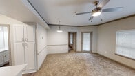 This well-designed one-bedroom, one-bathroom residence in Austin, TX offers a functional and comfortable single-floor layout. The living area features plush carpeting, a ceiling fan with light fixture, crown molding accents, and a pendant light overhead, creating a warm and inviting atmosphere. Natural light filters in through blinded windows and a glass-paneled door, providing pleasant outdoor views. The dedicated dining area is defined by a pendant light and a decorative chair rail, lending a structured yet casual feel. The galley-style kitchen is outfitted with white cabinetry, light countertops, a double-basin sink, and black appliances including an electric range and microwave. Wood-look vinyl flooring runs throughout the kitchen and bathroom, adding a cohesive, easy-care finish. A doorway off the kitchen provides access to an in-unit washer connection area for added convenience. The bedroom is a comfortable retreat with soft carpet, a ceiling fan, and a large window that brings in natural light. It connects directly to a walk-in closet equipped with wire shelving and a central storage unit, offering ample organization. The bathroom features wood-look flooring, a white vanity, tiled shower surround, and a clean, straightforward layout.