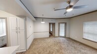 This well-designed one-bedroom, one-bathroom residence in Austin, TX offers a functional and comfortable single-floor layout. The living area features plush carpeting, a ceiling fan with light fixture, crown molding accents, and a pendant light overhead, creating a warm and inviting atmosphere. Natural light filters in through blinded windows and a glass-paneled door, providing pleasant outdoor views. The dedicated dining area is defined by a pendant light and a decorative chair rail, lending a structured yet casual feel. The galley-style kitchen is outfitted with white cabinetry, light countertops, a double-basin sink, and black appliances including an electric range and microwave. Wood-look vinyl flooring runs throughout the kitchen and bathroom, adding a cohesive, easy-care finish. A doorway off the kitchen provides access to an in-unit washer connection area for added convenience. The bedroom is a comfortable retreat with soft carpet, a ceiling fan, and a large window that brings in natural light. It connects directly to a walk-in closet equipped with wire shelving and a central storage unit, offering ample organization. The bathroom features wood-look flooring, a white vanity, tiled shower surround, and a clean, straightforward layout.