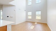 Located at 1657 Fairport Nine Mile Point Road in Penfield, NY, this two-story home offers a thoughtfully designed layout across two floors. The main level features an open-concept kitchen and living area with striking soaring ceilings that lend a sense of spaciousness. The kitchen is appointed with a central island featuring a white quartz countertop and integrated sink, warm wood cabinetry paired with crisp white upper cabinets, stainless steel appliances, and track lighting overhead. Light wood flooring flows seamlessly throughout the main level, complementing the neutral gray tones of the walls. Large windows invite abundant natural light and offer views of the surrounding greenery. The upper floor houses both bedrooms, including a generously sized primary bedroom with dramatic double-height windows that flood the room with light. The second bedroom features plush carpeting, multiple windows with outdoor views, and a double-door closet. Both bathrooms are well-appointed with warm wood vanities, white quartz countertops, large mirrors, and glass-enclosed showers, all finished with the same light wood-style flooring. Clean lines, neutral finishes, and an abundance of natural light define the overall ambiance of this well-designed home.