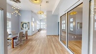 Located at 45 Nectaria Way in Manchester, New Hampshire, this single-floor amenity facility offers a thoughtfully designed space dedicated to fitness and community gathering. The building is accessed through a sleek glass-enclosed entryway with hardwood-style flooring that sets a clean, contemporary tone throughout.

The two exercise rooms are generously proportioned, featuring soaring ceilings, abundant natural light from multiple windows, and durable flooring suited for athletic use. Both rooms are outfitted with a comprehensive range of equipment, including treadmills, cable machines, multi-station weight systems, free weights, and benches, illuminated by striking tri-arm pendant light fixtures that add a modern design element overhead.

The lounge area impresses with dramatic vaulted ceilings, floor-to-ceiling windows, and a reclaimed wood accent wall anchoring a wall-mounted television. Comfortable sectional sofas and lounge chairs are arranged around the space, complemented by warm hardwood floors throughout. A shuffleboard table and a wet bar area provide additional entertainment options.

The meeting and dining area features soaring double-height ceilings, clerestory windows that flood the room with natural light, and a sculptural multi-bulb chandelier above a contemporary dining table. Glass-panel sliding doors connect to adjacent areas, enhancing the open flow of the facility.