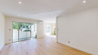 This single-floor unit offers a clean, modern aesthetic defined by light wood flooring, crisp white walls, and thoughtful design details throughout. The open living area is bathed in natural light, thanks to floor-to-ceiling sliding glass doors that lead to a private balcony overlooking lush, mature trees. A wall-mounted split air conditioning unit ensures year-round comfort. Recessed lighting complements the bright, airy atmosphere across the main living spaces.

The galley-style kitchen is a standout feature, showcasing vibrant olive-green lower cabinetry paired with white upper cabinets and white countertops. Stainless steel appliances — including a gas range, dishwasher, and refrigerator — are thoughtfully integrated, while a terrazzo-style floor adds a distinctive retro-modern touch. A window at the end of the kitchen brings in additional natural light.

The bedrooms continue the home's clean palette, with light wood flooring, white walls, and generous natural light from well-placed windows. Bold green-painted doors serve as a cohesive design accent throughout. One bedroom features a built-in shelving unit, adding practical storage.

The bathroom is finished with white square grid tiles on both the walls and floor, a soaker tub with overhead shower, a wood-toned vanity with a marble-look countertop, and a window for natural ventilation.