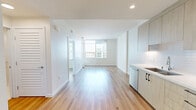 Located in the heart of San Diego's East Village at 1150 E Street, this thoughtfully designed one-bedroom, one-bathroom residence offers a clean, modern aesthetic throughout. Light-toned hardwood flooring flows seamlessly across the entire unit, complementing the bright white walls and recessed lighting that give the space an airy, open feel.

The open-concept living, dining, and kitchen area serves as the heart of the home. The kitchen is outfitted with flat-front, wood-grain cabinetry extending to the ceiling, white quartz countertops, a subway tile backsplash, and a full suite of stainless steel appliances including a French door refrigerator with ice maker, electric range, over-the-range microwave, and dishwasher. Floor-to-ceiling windows in the living area flood the space with natural light and frame elevated views of the San Diego skyline and surrounding cityscape.

The bedroom is a calm retreat featuring large windows with roller shades that capture sweeping city views. The bathroom is finished with marble-look tile flooring, a walk-in shower with coordinating tile surround, a wood-framed vanity with white countertop, and a mirrored medicine cabinet. Additional conveniences include a dedicated closet, in-unit laundry, and a private balcony.