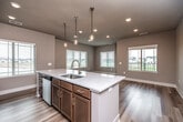 This well-appointed single-floor residence offers a thoughtfully designed open-concept layout that seamlessly connects the kitchen and living areas. The kitchen serves as the centerpiece of the home, featuring a large central island with a quartz countertop, an undermount sink, and elegant pendant lighting hanging above. Warm-toned wood cabinetry provides ample storage, while stainless steel appliances — including a refrigerator, electric range, and over-the-range microwave — complete the functional workspace. Light hardwood-style flooring flows throughout the main living areas, enhancing the bright and airy atmosphere created by multiple windows fitted with blinds that invite natural light throughout the day.

The living area offers generous open space with views to the outdoors through large windows. Bedrooms are finished with plush carpeting and ceiling fans, providing comfort and practicality. One bedroom features direct sightlines to the kitchen, maintaining the home's connected feel. A full bathroom includes a tub-shower combo with clean white surround, wood-look flooring, and brushed nickel fixtures. Storage is well addressed with a dedicated walk-in closet outfitted with wire shelving. The textured ceilings and neutral warm-gray wall tones throughout create a cohesive, modern, and welcoming interior.