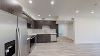 Located on Hartsook Street in the North Hollywood neighborhood of Los Angeles, this single-floor unit showcases a clean, contemporary design throughout. Light wood-style flooring flows consistently across the open living areas, creating a cohesive and airy feel.

The kitchen is a standout feature, outfitted with dark espresso-toned cabinetry, white quartz countertops, and a full suite of stainless steel appliances including a French door refrigerator, range, microwave, and dishwasher. Recessed lighting illuminates the space efficiently, while the open layout allows the kitchen to connect seamlessly to the living area.

The living space is bright and generously proportioned, with neutral white walls and large windows fitted with vertical blinds that invite natural light and offer outdoor views of surrounding greenery.

The primary bathroom is notably refined, featuring marble-look tile flooring, a dual-sink vanity with dark wood cabinetry and white quartz surfaces, a glass-enclosed shower with marble surround, and direct access to a built-in walk-in closet with dedicated shelving and drawer storage. The overall ambiance of the unit is modern, clean, and move-in ready.