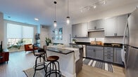 This efficiently designed one-bedroom, one-bathroom residence offers a thoughtful layout that maximizes every square foot across a single floor. The open-concept kitchen and living area serves as the heart of the home, featuring gray shaker-style cabinetry, dark granite countertops, and a full suite of stainless steel appliances including a refrigerator, range, microwave, and dishwasher. A central island with a matching granite top provides additional prep space and casual bar seating beneath stylish pendant lighting, while track lighting overhead adds further illumination. Light wood-tone flooring runs throughout the main living area, lending warmth and visual continuity. The living room receives generous natural light through a large window and offers ample space for comfortable seating arrangements. The bedroom is a calm, carpeted retreat with a window that brings in natural light and outdoor views. It connects to a dedicated walk-in closet equipped with wire shelving for organized storage. The bathroom features a gray vanity with a white countertop, wood-tone flooring, and a shower-tub combination. Clean white walls and neutral tones throughout create a bright, modern ambiance that is both functional and inviting.
