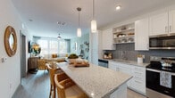 This single-story residence is thoughtfully designed with an open-concept layout that seamlessly connects the kitchen, dining, and living areas. The kitchen serves as a central hub, featuring white shaker-style cabinetry, open shelving, and a granite-topped island with bar seating illuminated by modern pendant lighting. A herringbone-patterned tile backsplash adds visual interest, while stainless steel appliances — including a refrigerator, range, microwave, and dishwasher — provide full functionality. Light wood-tone flooring runs throughout the main living areas, contributing to a clean, cohesive aesthetic.

The living area is bright and inviting, with large windows that frame outdoor views of greenery and allow generous natural light to fill the space. A ceiling fan enhances comfort, and the layout comfortably accommodates a full sectional seating arrangement.

The bedroom offers a calm retreat with soft accent wall tones, large windows with views to the outdoors, a ceiling fan, and access to a dedicated walk-in closet with wire shelving for organized storage.

The bathroom is finished with a granite-topped vanity, large-format tile flooring, and a soaking tub framed by striking marble-look tile surround, lending a polished, spa-like quality to the space.
