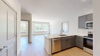 This well-designed 2-bedroom, 2-bathroom residence in Oxford, Mississippi offers a bright and contemporary living experience across a single floor. The open-concept kitchen and living area serves as the heart of the home, anchored by a large quartz-topped island with an undermount sink. The kitchen is outfitted with gray shaker-style cabinetry, a subway tile backsplash, and a full suite of stainless steel appliances including a refrigerator, range, microwave, and dishwasher. Light wood-style flooring flows seamlessly throughout the entire unit, enhancing the clean, modern aesthetic. Large windows in the living area and bedrooms invite abundant natural light and offer views of the surrounding greenery. The primary bedroom is a comfortable retreat featuring a walk-in closet with wire shelving and a private en-suite bathroom with a dual-tone vanity, white quartz countertop, and a shower-tub combination. The second bedroom is equally well-lit with generous window coverage and convenient closet access. A second full bathroom serves the remaining spaces. Neutral white walls and raised-panel interior doors complete the polished, move-in-ready design of this Oxford residence.