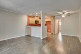 Located at 2828 W Ball Rd in Anaheim, California, this single-floor unit offers a well-organized and functional layout designed for comfortable living. The open-concept living and dining area is finished with rich hardwood-style flooring that runs throughout the main living spaces, complemented by crown molding and a ceiling fan overhead. Natural light filters in through a sliding glass door at the front, which opens to a private outdoor balcony area. A half-wall partition separates the living area from the kitchen, creating a semi-open feel while defining each space. The kitchen is well-equipped with light maple cabinetry, dark granite-style countertops, black appliances including a range, microwave, and dishwasher, and recessed lighting set against a bold terracotta accent wall that adds warmth and character. The bedroom is carpeted and features a ceiling fan, ample wall space, and a sliding glass door with vertical blinds that leads to an outdoor area, allowing for natural light and ventilation. The bathroom includes a vanity with a dark granite countertop, a single-basin sink, wood cabinetry, and brushed nickel fixtures, alongside a tub and toilet. Hardwood-style flooring continues into the bathroom, tying the unit's design together cohesively.