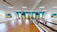 Located at 1851 SR-59 in Kent, Ohio, this single-floor fitness studio is a well-appointed, energetic space designed to accommodate a variety of group exercise and individual workout activities. The studio's most striking design feature is its bold geometric wall mural, composed of large triangular shapes in teal, lime green, black, and white, which creates a dynamic and motivating atmosphere throughout the room.

The expansive main workout area is finished with warm hardwood-style flooring, providing both aesthetic appeal and a practical surface for a range of fitness activities. Full-length mirrors run along one wall, visually enlarging the space and allowing participants to monitor their form during exercise. A freestanding barre system is positioned in front of the mirrors, supporting dance, barre, and stretching classes.

The studio is equipped with multiple stationary cycling bikes arranged for group spin sessions, as well as an assortment of fitness accessories including medicine balls and stability balls, which are neatly organized on wall-mounted shelving. Flat-screen televisions are mounted at multiple points throughout the room to facilitate instructor-led or media-guided workouts.

Natural light filters in through several windows, complemented by recessed and flush-mounted ceiling lighting. Ceiling fans help maintain comfortable airflow during high-intensity sessions. The overall ambiance is bright, clean, and purpose-built for fitness.