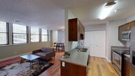 Located at 26 Sheldon Blvd SE in the heart of Grand Rapids, Michigan, this single-floor residence offers a thoughtfully designed layout that balances comfort and functionality. The open-concept living and dining area is anchored by warm hardwood flooring and neutral gray walls, creating a bright and welcoming atmosphere. Large windows in the dining nook allow natural light to fill the space while offering views of the surrounding downtown cityscape.

The galley-style kitchen is well-appointed with rich, dark-stained wood cabinetry, gray quartz-style countertops, stainless steel appliances — including a refrigerator, range, and microwave — and a double-basin sink set into a center peninsula. Ample upper and lower cabinet storage makes this kitchen as practical as it is attractive.

Two bedrooms provide comfortable retreats, each featuring plush carpeting, neutral-toned walls, and closet access via paneled doors. The unit includes two full bathrooms, both finished with stone-tile flooring, a tub-shower combination, a wood-framed vanity mirror, and a single-sink vanity with light countertops. The consistent use of warm wood tones and cool gray hues throughout the unit creates a cohesive and modern aesthetic suited for urban living.