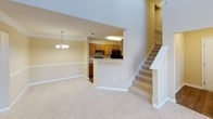 This two-story residence offers a well-organized layout across both levels, beginning with a welcoming main floor characterized by an open living and dining area. The living space features dramatic double-height ceilings flooded with natural light from tall windows and an upper transom, creating a notably airy atmosphere. Crown molding and a chandelier in the dining area add a refined touch, while plush carpeting runs throughout. A carpeted staircase with a white-painted banister connects both floors.

The kitchen is laid out in a galley configuration, equipped with warm honey-toned cabinetry, light laminate countertops, black appliances including a refrigerator and electric range, and durable hardwood-style flooring. A pass-through opening connects it to the living area, enhancing the open flow.

Upstairs, the bedrooms are carpeted and finished in neutral tones. One features a ceiling fan, a large window with exterior views, and generous closet space. Another upstairs room opens to an interior overlook, offering a unique architectural view of the main level below. A full bathroom is outfitted with a white tub and shower combination and hardwood-style flooring. An additional room with a textured ceiling and utility panel provides flexible use as storage or a bonus space.