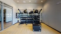 Located at 1200 Allison Dr in Vacaville, CA, this single-level Fitness Center and Yoga Room offers a comprehensive workout facility designed to support a wide range of exercise routines. The space is divided into distinct functional zones, each thoughtfully outfitted with professional-grade equipment.

The main fitness area features rubber flooring and houses a dual-cable functional trainer, a multi-tier strength rack stocked with kettlebells, medicine balls, stability balls, resistance bands, TRX suspension trainers, and plyometric boxes. Full-length wall mirrors enhance the sense of space and allow for form monitoring during workouts. Recessed lighting and a drop tile ceiling give this zone a clean, polished aesthetic.

An adjacent yoga and cycling studio is separated from the main gym by floor-to-ceiling glass partition walls with wide aluminum-framed glass doors, providing visual connectivity while maintaining acoustic separation. This bright, open room features light wood-tone flooring, large windows that invite natural light and outdoor views, and wall-mounted mirrors. Spin bikes are positioned facing the mirrors, with a wall-mounted flat-screen television overhead for guided sessions.

The combination of natural light, mirrored walls, modern finishes, and varied flooring surfaces creates a motivating and versatile environment suited for cardio, strength, flexibility, and group fitness training.