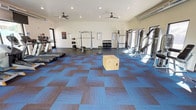 This single-floor fitness center offers a well-organized and fully equipped workout environment designed to accommodate a wide range of exercise routines. The open layout provides ample space for movement and training, with a distinctive patterned carpet tile floor in shades of blue and brown that adds both visual interest and functional cushioning underfoot.

The cardio zone features treadmills positioned along one side of the room, while the strength training area is thoughtfully arranged with a power rack, a multi-station cable machine, an adjustable bench, and a dedicated dumbbell rack stocked with a range of weights. A wooden plyo box positioned in the center of the floor highlights the space's versatility for functional fitness and high-intensity training.

The room is illuminated by recessed ceiling lights supplemented by natural light streaming in through large windows and a glass door on one side, creating a bright and energizing atmosphere. Two ceiling fans are mounted overhead to ensure consistent air circulation throughout the space.

The walls are finished in a clean, neutral tone, keeping the environment focused and distraction-free. Informational signage and instructional posters are displayed on the walls, offering guidance and safety reminders. Overall, this fitness center is a practical, well-appointed space suited for a comprehensive fitness regimen.
