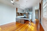 Located at 427 Josephine Street in New Orleans' Lower Garden District, this one-bedroom, two-bathroom unit artfully merges historic architectural character with contemporary updates. The open-concept living and kitchen area immediately draws the eye with its rich, wide-plank reclaimed hardwood floors that catch natural light streaming through large windows framed against dramatic exposed brick walls. Original heavy timber columns punctuate the space, reinforcing its industrial-historic charm. The kitchen features dark wood cabinetry, stainless steel appliances including a refrigerator and microwave, a gas range, and a generous granite-topped island with pendant lighting overhead — ideal for both cooking and casual dining. Soaring ceilings with ceiling fans enhance the sense of openness throughout. The bedroom continues the exposed brick aesthetic, offering a spacious and characterful retreat. Both bathrooms are finished with classic black-and-white octagonal tile flooring, white vanity cabinetry, granite countertops, and well-lit mirrors, with one bathroom featuring a full soaking tub and shower combination. A dedicated closet and hallway round out the practical layout. This unit delivers an authentic New Orleans loft experience, balancing the building's storied past with refined, modern livability.