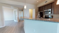 This thoughtfully designed 2-bedroom, 2-bathroom residence is laid out across a single level, making excellent use of its generous floor plan. The open-concept kitchen serves as a central highlight, featuring rich dark cabinetry, granite countertops, a sleek breakfast bar peninsula, and stainless steel appliances including a refrigerator, range, and built-in microwave. A stylish pendant light fixture hangs above the peninsula, adding a touch of modern elegance to the space. The kitchen flows naturally into the main living area, which is finished with durable wood-style plank flooring that extends throughout the unit. The neutral wall tones and recessed lighting create a bright, welcoming ambiance. A hallway leads to the two bedrooms, each offering privacy and functionality. Both bathrooms are conveniently accessible, supporting the home's practical layout. Visible throughout are clean architectural lines, ample cabinetry storage, and thoughtful details that contribute to a polished, contemporary feel. The overall design balances comfort and style, making this a well-appointed and move-in-ready living space.