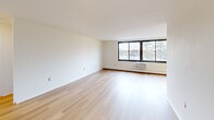 Located on the fourth floor at 1 Highgate Drive in Ewing, NJ, Unit 407 is a one-bedroom, one-bathroom residence offering a clean, functional layout with bright, neutral interiors throughout. The spacious living room is a standout feature, showcasing light-toned hardwood flooring, crisp white walls, and a large picture window that frames outdoor views and fills the room with natural light. A wall-unit air conditioner and baseboard heating provide year-round climate comfort. An adjacent area reveals a ceiling fan and glimpse of dark-cabinetry kitchen, adding to the unit's practical flow. The generously sized bedroom is carpeted for warmth and comfort, featuring its own large window with outdoor views, a wall-unit AC, and an expansive built-in closet with full-width bi-fold doors offering abundant storage. The bathroom includes a full soaking tub with an overhead shower, accented by classic white square tile and subtle tan tile detailing along the walls. Throughout the unit, the consistent use of white walls, light flooring, and well-placed windows creates a bright, airy ambiance that feels open and move-in ready.