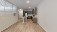 This single-floor residence offers a well-designed layout that balances functionality and modern aesthetics throughout. The open-concept kitchen serves as a central highlight, outfitted with stainless steel appliances including a refrigerator, electric range, and over-the-range microwave. Warm-toned, wood-grain cabinetry extends from floor to ceiling, complemented by open upper shelving and light granite-style countertops. A kitchen island with a built-in sink provides additional prep space and acts as a natural divider between the kitchen and the adjoining living area. Light hardwood-style flooring flows consistently throughout the main living spaces, lending a clean and cohesive feel to the interior. The living area is bright and airy, benefiting from multiple windows fitted with horizontal blinds that invite natural light while maintaining privacy. A private entrance door from this area adds a practical touch. The bedroom, accessible through a wide doorway, features carpeted flooring and a ceiling fan, creating a comfortable retreat. The bathroom is clean and straightforward, featuring a tiled soaking tub and shower combination, hardwood-style flooring, and a simple, functional layout. Neutral wall tones throughout the space provide a versatile backdrop, making it easy to personalize and furnish to individual taste.
