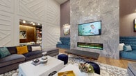 This contemporary amenity space is designed with a bold, curated aesthetic that balances sophistication with comfort. The centerpiece of the main lounge is a dramatic floor-to-ceiling marble-clad accent wall, which frames a large flat-screen television and a sleek linear electric fireplace, creating a striking focal point. Soaring double-height ceilings amplify the sense of openness throughout, while wide-plank hardwood flooring adds warmth underfoot.

Seating is thoughtfully arranged to encourage both socializing and relaxation, featuring plush gray sofas, velvet teal banquette seating, and accent ottomans. A geometric white paneled wall provides an architectural contrast to the textured stone surfaces, and curated artwork is displayed throughout. Pendant lighting with a mixed-metal finish adds an upscale touch to the bar area, which features a white quartz countertop with wood-paneled base and bar-height seating — framed by large black-trimmed windows overlooking an outdoor pool courtyard.

A separate utility kitchen includes white shaker cabinetry, a subway tile backsplash, stainless steel appliances, and hexagonal tile flooring. Tucked seating nooks with teal upholstered benches and wall-mounted art offer quieter retreats within the space. The overall ambiance is modern, vibrant, and welcoming.
