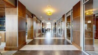 This single-story space is designed with a contemporary aesthetic, combining warm wood paneling, large-format dark tile flooring, and modern finishes throughout. The main corridor serves as an impressive entry point, lined with rich walnut-toned wall panels accented by aluminum trim and floor-to-ceiling glass partitions that allow views into adjacent rooms. Decorative drum pendant lighting punctuates the hallway, adding warmth to the polished interior.

The lounge area features soaring double-height ceilings with expansive floor-to-ceiling windows that flood the space with natural light and provide views of the surrounding landscaping. Stylish seating, a wall-mounted television, and curated décor create an inviting, well-appointed gathering space.

The kitchen is fully equipped for event use, featuring stainless steel appliances, a professional-grade range with a stainless hood, quartz countertops, warm wood cabinetry, and a textured tile backsplash. A wall of windows brings in abundant natural light and outdoor views.

A glass-enclosed sunroom offers a relaxed retreat with wraparound windows overlooking mature trees and garden beds, complemented by a generous sectional sofa and a wood-paneled ceiling that adds a natural, organic element to the space.