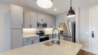 Located at 700 Corporate Center Dr in Raleigh, NC, this thoughtfully designed single-floor residence offers a contemporary living experience with high-quality finishes throughout. The open-concept kitchen serves as the heart of the space, anchored by a granite-topped island with an undermount sink and matte black faucet, illuminated by striking industrial-style pendant lights. Gray shaker-style cabinetry with matte black hardware lines the walls, complemented by a herringbone tile backsplash, under-cabinet lighting, and a full suite of stainless steel appliances including a range, microwave, and French door refrigerator. Light wood-look flooring flows seamlessly throughout the main living areas, adding warmth and cohesion. A standout architectural detail is the sliding barn door, which leads into a private suite complete with a bathroom featuring granite countertops, dual-sink vanity with framed mirror, and dark hardware accents. The walk-in closet provides generous built-in shelving and hanging space with dark hardwood-style flooring. Clean white walls, recessed lighting, and crisp trim work give the entire space a bright, polished ambiance well-suited for modern living.