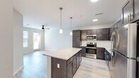 This thoughtfully designed 1-bedroom, 1-bathroom residence offers a comfortable and functional layout across a single floor. The open-concept kitchen and living area serves as the heart of the unit, featuring rich dark-stained cabinetry, granite countertops, a classic white subway tile backsplash, and a full suite of stainless steel appliances including a refrigerator, range, microwave, and dishwasher. A granite-topped kitchen island provides additional prep space and casual seating. Pendant lighting illuminates the kitchen, while a ceiling fan keeps the living area comfortable. Light wood-look flooring flows throughout the main living spaces, adding a clean, modern aesthetic. A sliding glass door in the living room fills the space with natural light and provides outdoor access. The spacious primary bedroom features soft carpeting underfoot, a ceiling fan, and access to both a full bathroom and a dedicated laundry room equipped with a full-size washer and dryer. The bathroom includes a full tub-shower combination with brushed nickel fixtures. A walk-in closet with wire shelving adds practical storage. Neutral tones and clean lines throughout create a bright, move-in-ready atmosphere suited for contemporary living.