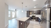 This thoughtfully designed 1-bedroom, 1-bathroom residence offers a comfortable and functional layout across a single floor. The open-concept kitchen and living area serves as the heart of the unit, featuring rich dark-stained cabinetry, granite countertops, a classic white subway tile backsplash, and a full suite of stainless steel appliances including a refrigerator, range, microwave, and dishwasher. A granite-topped kitchen island provides additional prep space and casual seating. Pendant lighting illuminates the kitchen, while a ceiling fan keeps the living area comfortable. Light wood-look flooring flows throughout the main living spaces, adding a clean, modern aesthetic. A sliding glass door in the living room fills the space with natural light and provides outdoor access. The spacious primary bedroom features soft carpeting underfoot, a ceiling fan, and access to both a full bathroom and a dedicated laundry room equipped with a full-size washer and dryer. The bathroom includes a full tub-shower combination with brushed nickel fixtures. A walk-in closet with wire shelving adds practical storage. Neutral tones and clean lines throughout create a bright, move-in-ready atmosphere suited for contemporary living.