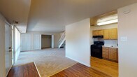 This two-floor space is designed with a practical, functional layout that makes efficient use of its square footage. The main level opens into a generously sized living area finished with neutral-toned carpet, which transitions to hardwood-style flooring near the entry and kitchen zones. Large sliding glass doors flood the living space with natural light while providing a view of surrounding greenery and direct access to an outdoor area. A white staircase with open railings connects the main level to the upper floor, serving as a central architectural feature.

The kitchen is semi-open to the living area, separated by a partial wall. It features warm oak cabinetry with ample upper and lower storage, light-toned countertops, a stainless steel sink, and a black gas range with an overhead ventilation hood. Hardwood-style flooring continues throughout the kitchen.

The main level also includes a closet area, while the upper floor houses multiple carpeted bedrooms. Each bedroom is well-proportioned, with neutral walls and bifold closet doors offering organized storage. One bedroom features a wide window with outdoor views. The bathroom includes a full tub-shower combination, a wood-toned vanity with granite-style countertop, and white tile flooring throughout.