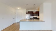 This single-floor residence is designed with a clean, contemporary aesthetic and a functional open-concept layout. The kitchen serves as a central highlight, featuring rich dark-wood cabinetry, granite countertops, and a full suite of stainless steel appliances, including a refrigerator, electric range, and microwave. A generously sized peninsula with a built-in sink and granite surface extends into the living area, illuminated by a pair of sleek pendant lights. Light wood-style flooring runs throughout the main living areas, lending warmth and continuity to the space.

The living room is bright and open, benefiting from natural light that enters through a sliding glass door leading to an outdoor patio. A ceiling fan adds comfort to the airy space. The bedrooms are carpeted, offering a softer feel, and each includes windows fitted with blinds that allow for controlled natural light.

Two bathrooms serve the unit. One features a walk-in shower with a dark-wood vanity and granite countertop, while the second includes a shower-tub combination. Both bathrooms are finished with light tile flooring and chrome fixtures. The overall palette throughout the unit is neutral and bright, creating a clean, move-in-ready atmosphere.