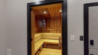 Located in Savannah, GA, this dedicated sauna facility offers a refined wellness retreat designed with both function and aesthetics in mind. The centerpiece is a stunning cedar-lined sauna room, accessed through a sleek black-framed glass door. Inside, warm natural wood covers every surface — from the slatted tiered benches arranged in an L-shape to the paneled walls and ceiling — creating an inviting, heat-retaining environment. Recessed lighting embedded in the cedar ceiling casts a warm, golden glow throughout the interior, enhancing the natural richness of the wood tones.

The anteroom serves as a thoughtful transitional space, featuring large-format dark slate tile flooring, a built-in bench set against a bold black brick accent wall, and a decorative area rug. This cooling area provides a comfortable place to relax before or after a sauna session. A full-length mirror and curated silhouette artwork displayed along the corridor walls add a distinctive, artistic character to the space.

The overall design balances modern industrial elements — dark door frames, matte black hardware, and slate tile — with the organic warmth of natural cedar, resulting in a cohesive and sophisticated wellness environment.