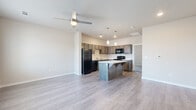This single-story residence offers a thoughtfully designed 1-bedroom, 1-bathroom layout that maximizes its footprint through an open-concept floor plan. Light-toned luxury vinyl plank flooring flows throughout the main living areas, complemented by neutral wall tones that create a clean, modern aesthetic.

The living room is bright and welcoming, featuring a ceiling fan, multiple windows with blinds that allow natural light to filter in, and easy access to the front entry. It connects seamlessly to the kitchen, which serves as a functional centerpiece of the home. The kitchen is equipped with rich, dark-toned cabinetry extending to the upper walls, white countertops, a full suite of black appliances including a refrigerator, range, microwave, and dishwasher, and a peninsula island with additional counter space — all illuminated by pendant lighting overhead.

The bedroom offers a comfortable, carpeted retreat with a walk-in closet providing generous storage. A full bathroom is conveniently located nearby, featuring a single-sink vanity with dark wood cabinetry, a white countertop, a mirror, and a tub-shower combination. A dedicated closet space rounds out the unit's storage options. The overall design balances practicality with contemporary style, making efficient use of every room.