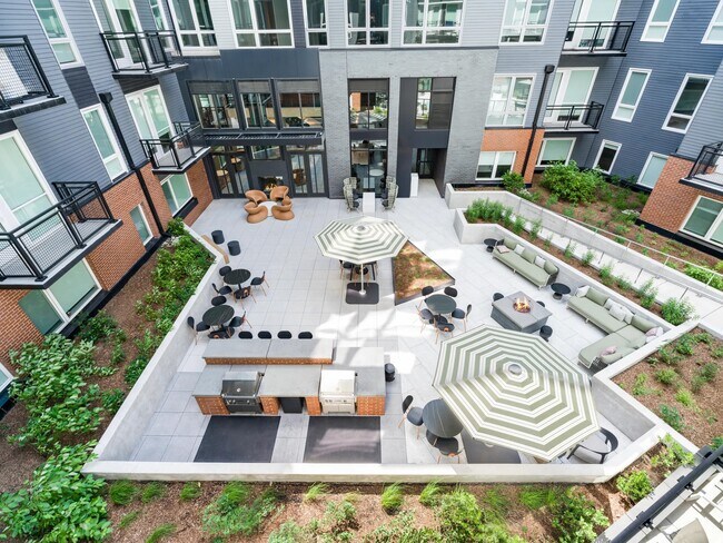 Patio interior con zona de estar, mesas de café y zonas de barbacoa dispuestas alrededor de jardineras ajardinadas para disfrutar del aire libre en compañía. - Modera H Street