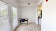 Located in Tallahassee, FL, this efficient one-bedroom, one-bathroom unit offers a practical and functional layout across a single floor. The bedroom features neutral, light-colored walls, carpeted flooring, a ceiling fan, and a louvered closet, providing a comfortable and organized personal space. The living area extends the functionality of the unit with carpeted flooring, a large window fitted with blinds that allows ample natural light to filter in, and convenient access to a compact kitchenette equipped with a mini-refrigerator and microwave. A dedicated entrance door leads directly into this space, adding privacy and accessibility. The bathroom is well-appointed with a full tub and shower combination featuring white subway tile surround, a grab bar for added safety, a toilet, and a vanity topped with a dark granite-style countertop and an integrated sink, complemented by a large mirror and tile flooring. The unit's clean white walls and neutral tones throughout create a simple, cohesive aesthetic that is easy to personalize. Overall, the space is thoughtfully designed to maximize utility within a compact footprint, making it a practical option in the Tallahassee area.