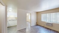 This 2-bedroom, 1-bathroom apartment offers 360 square feet of efficiently designed single-floor living space. The unit features consistent wood-look laminate flooring throughout, lending a cohesive and clean aesthetic across all rooms. The primary bedroom measures 230 square feet and is equipped with a ceiling fan with light fixture, wall sconces, vertical blind-covered windows that allow natural light, and a built-in closet with a hanging rod and integrated lighting. The second bedroom also includes a ceiling fan with lighting, a large window with vertical blinds offering outdoor views, and a wall-mounted HVAC unit for individualized climate control. The kitchen is positioned at the front of the unit and features white cabinetry, a refrigerator, and a sink with an open pass-through layout. The bathroom is finished in a clean, all-white palette with a tiled shower-tub combination, a white vanity with cabinet storage, and chrome fixtures. Neutral beige walls throughout the unit contribute to a bright and open feel, while the wood-look flooring and functional layouts make this apartment a practical and straightforward living space suitable for those seeking simplicity and efficiency.