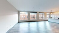 Located at 205 S High St in the heart of downtown Columbus, Ohio, this thoughtfully designed one-bedroom, one-bathroom unit offers a refined urban living experience across a single floor. The spacious living room immediately impresses with a row of large, black-framed grid-pane windows that flood the space with natural light and frame views of the surrounding historic brick architecture. Light-toned luxury vinyl plank flooring runs throughout, complementing the clean, neutral color palette. A striking set of glass-paneled French doors connects the bedroom to the main living area, adding an elegant architectural touch. The kitchen is well-appointed with white shaker cabinetry, granite countertops, a subway tile backsplash, stainless steel appliances including a refrigerator and range, and a central island with a sink — ideal for both cooking and entertaining. The bedroom is a comfortable, well-lit retreat with its own grid-pane window and continuity of the modern flooring. The bathroom features classic white subway tile surrounding a soaking tub with a rain showerhead, a white vanity with ample storage, and clean tile flooring. A dedicated laundry room accommodates a full-size washer and dryer, adding everyday convenience to this polished downtown residence.