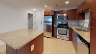 Located at 460 River in Andover, Massachusetts, this two-floor residence offers an impressive blend of modern design and functional living. The main level immediately captivates with its dramatic double-height ceilings in the open-concept living area, complete with a ceiling fan overhead and a mezzanine-style overlook from the upper floor. Plush carpeting runs throughout the living spaces, lending warmth to the expansive layout. The kitchen is well-appointed with rich wood cabinetry, granite countertops, stainless steel appliances including a gas range, microwave, and refrigerator, and a central island that doubles as a breakfast bar. Light tile flooring ties the kitchen together seamlessly. A clean, well-lit bathroom on the main level features matching wood vanity cabinetry and tile flooring. Upstairs, the upper level offers generously sized bedrooms bathed in natural light from large windows with exterior views. The primary bedroom is accompanied by a spacious walk-in closet with built-in shelving and a full en-suite bathroom featuring a dual-sink vanity with granite countertops. A dedicated in-unit laundry room with full-size washer and dryer adds everyday convenience. The vaulted ceilings on the upper level further enhance the sense of openness throughout this well-designed residence.