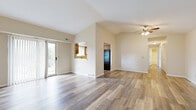 This single-floor residence offers a thoughtfully designed layout with a warm, neutral color palette throughout. The open living area immediately impresses with its vaulted ceilings that lend a sense of spaciousness and airiness. Wood-look laminate flooring flows across the main living spaces, complementing the light beige walls and clean white trim. A ceiling fan with light fixture anchors the living area, while a sliding glass door with vertical blinds invites natural light and provides access to the outdoors.

The kitchen features warm oak cabinetry with ample upper and lower storage, a double-basin sink positioned beneath a window, white countertops, and black appliances including a gas range, dishwasher, and refrigerator. A convenient pass-through window connects the kitchen to the living area, enhancing the open feel of the space.

The bedrooms are carpeted for comfort and each includes a ceiling fan, a window with blinds allowing natural light and outdoor views, and generous wall space. The bathroom is well-appointed with wood-look flooring, a combined tub and shower, a wood-toned vanity with a single sink, and brushed nickel fixtures. A hallway connects the private areas of the home, completing this practical and inviting floor plan.