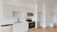 This well-designed one-bedroom, one-bathroom unit offers a clean, modern aesthetic throughout, characterized by an all-white color palette, light wood-tone flooring, and an abundance of natural light. The open-concept layout seamlessly connects the kitchen and living area, creating a spacious and airy feel despite its efficient footprint.

The kitchen is thoughtfully designed with sleek white flat-panel cabinetry extending to the ceiling for ample storage, complemented by a full suite of stainless steel appliances including a refrigerator, electric range, built-in microwave, and dishwasher. A matte black faucet adds a contemporary contrast over the single-basin sink.

The living area benefits from large windows that frame outdoor views of the surrounding cityscape and distant hills, with natural light filling the space throughout the day. The bedroom is generously sized with a ceiling fan, large windows with scenic views, and direct access to a dedicated closet.

The bathroom features a warm wood-toned vanity with ample drawer storage, a white quartz countertop, an undermount sink with brushed gold fixtures, a large mirror, and a glass-enclosed shower adorned with elegant marble-style tile. Light wood flooring carries through the bathroom, tying together the cohesive design of the unit.