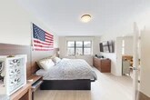 Located at 1030 E Genesee St in Syracuse, NY, this well-appointed 2-bedroom, 2-bathroom residence offers a thoughtfully organized single-floor layout. The space features light wood-tone flooring throughout, creating a cohesive and modern aesthetic.

The spacious primary bedroom receives generous natural light through large windows and features a warm walnut-toned headboard wall panel, providing a contemporary focal point. A wall-mounted TV and dresser complete the room's functional design. The second bedroom, also generously sized, offers built-in accent lighting along the headboard wall, adding a distinctive ambiance.

Both bathrooms are finished with neutral stone-look tile flooring. The full bathroom includes a backlit vanity mirror, white cabinetry with clean-line hardware, and a shower-tub combination. The second bathroom is finished with similar tile and a shower enclosure.

The kitchen is efficiently designed with white shaker-style cabinetry extending to the ceiling for ample storage, light stone countertops, and a full suite of stainless steel appliances including a refrigerator, dishwasher, range, and microwave.

The open living area provides flexible space, with direct sightlines to the bathroom and adjacent rooms. Three closets throughout the unit offer practical storage solutions, rounding out this well-designed Syracuse residence.