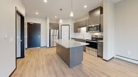 Located at 220 Benson Ave SW in Willmar, Minnesota, this well-appointed single-floor residence offers a thoughtfully designed layout with modern finishes throughout. The open-concept kitchen serves as the heart of the space, showcasing rich dark cabinetry, granite countertops, a central island with pendant lighting, and a full suite of stainless steel appliances including a refrigerator, range, microwave, and dishwasher. A crisp subway tile backsplash adds a clean, contemporary touch. Light wood-look flooring flows seamlessly through the main living and kitchen areas, complementing the neutral warm-toned walls. The living area is generously proportioned, featuring a wall-mounted air conditioning unit, baseboard heating, and a sliding glass door that opens onto a private balcony with outdoor views. The bedroom offers plush carpeting, a ceiling fan, a large window with natural light, and baseboard heating for year-round comfort. The bathroom is finished with a wide granite-topped vanity, dark cabinetry with brushed nickel hardware, a large mirror, and light flooring. An adjacent walk-in closet provides ample storage. Recessed lighting throughout adds to the clean, modern ambiance of this well-designed residence.